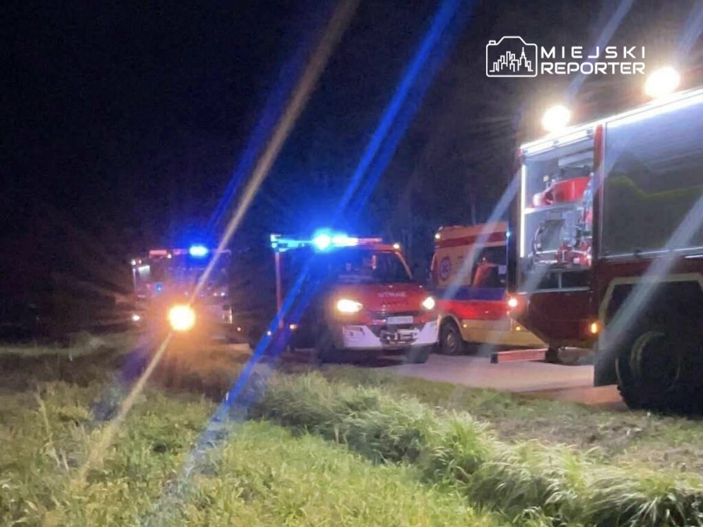 W nocy na drodze stoją pojazdy służb ratunkowych z włączonymi sygnałami świetlnymi.