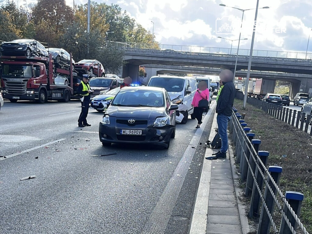 Policjant zbiera informacje na miejscu kolizji drogowej na ruchliwej ulicy, a w tle widać zablokowany ruch.