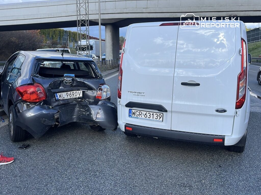 Czarny samochód osobowy z uszkodzoną tylną częścią stoi na drodze obok białego vana.