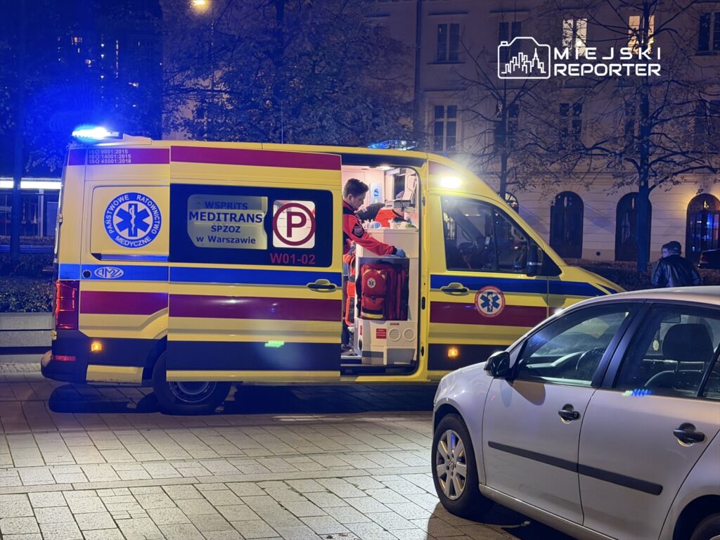 Karetka pogotowia z włączonymi sygnałami świetlnymi stoi na ulicy, a ratownik przygotowuje sprzęt medyczny.