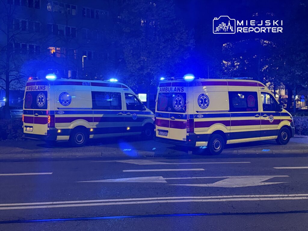 Dwa karetki pogotowia z włączonymi sygnałami świetlnymi zaparkowane w nocy na ulicy.