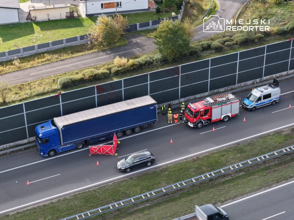 Zespół ratunkowy pracuje przy niebieskiej ciężarówce na poboczu drogi, otoczonej pachołkami.