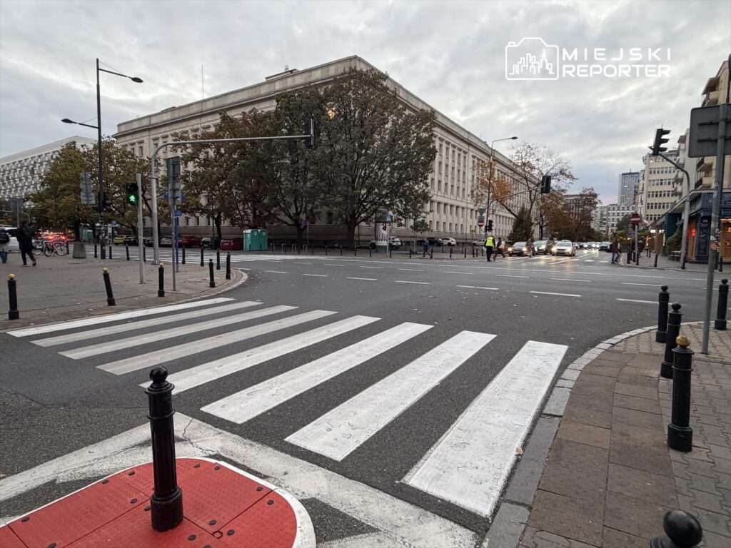 Zielone światło na sygnalizatorze, pieszy zbliżający się do przejścia dla pieszych w miejskim otoczeniu.