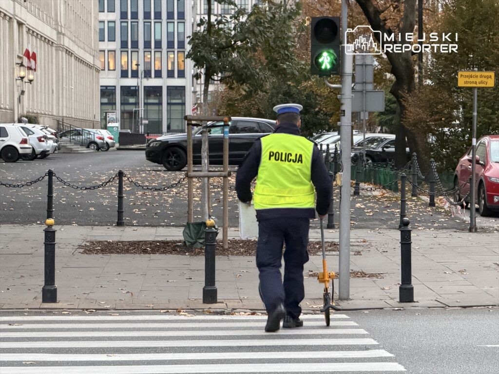 Policjant w odblaskowej kamizelce mierzy długość ulicy przy zielonym świetle dla pieszych.
