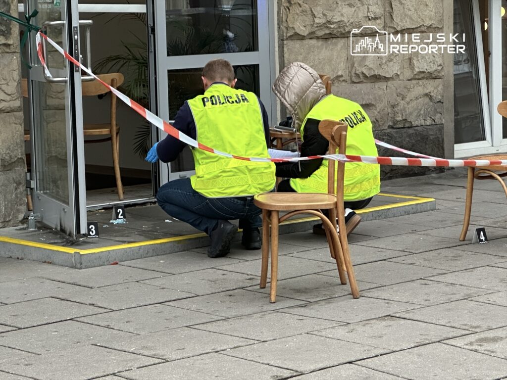 Funkcjonariusze policji zabezpieczają miejsce zdarzenia przed wejściem do lokalu, analizując ślady na chodniku.