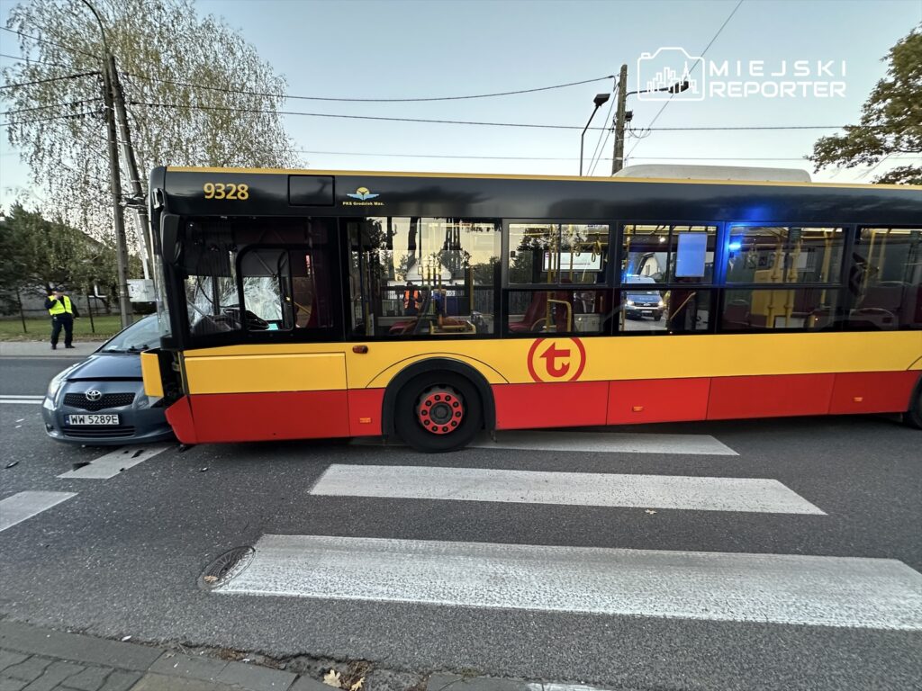 Autobus komunikacji miejskiej z numerem 9328 zatrzymany na przejściu dla pieszych obok uszkodzonego samochodu osobowego.