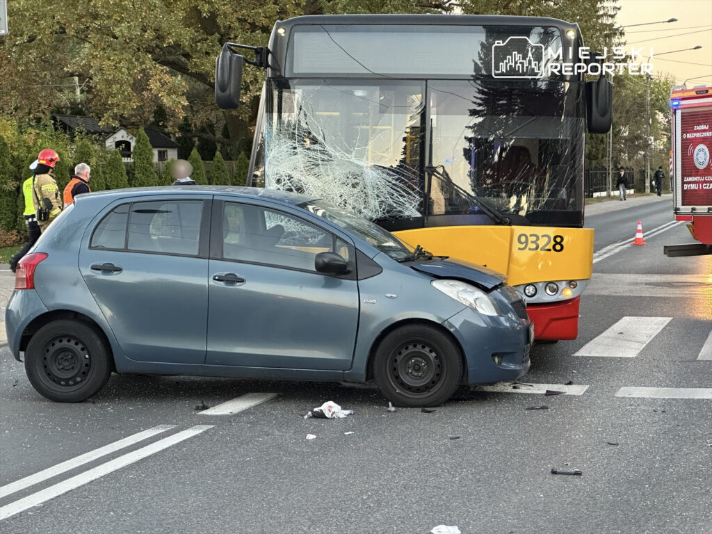 Wypadek drogowy z udziałem autobusu miejskiego i osobowego samochodu na skrzyżowaniu, wokół pracownicy służb ratunkowych.