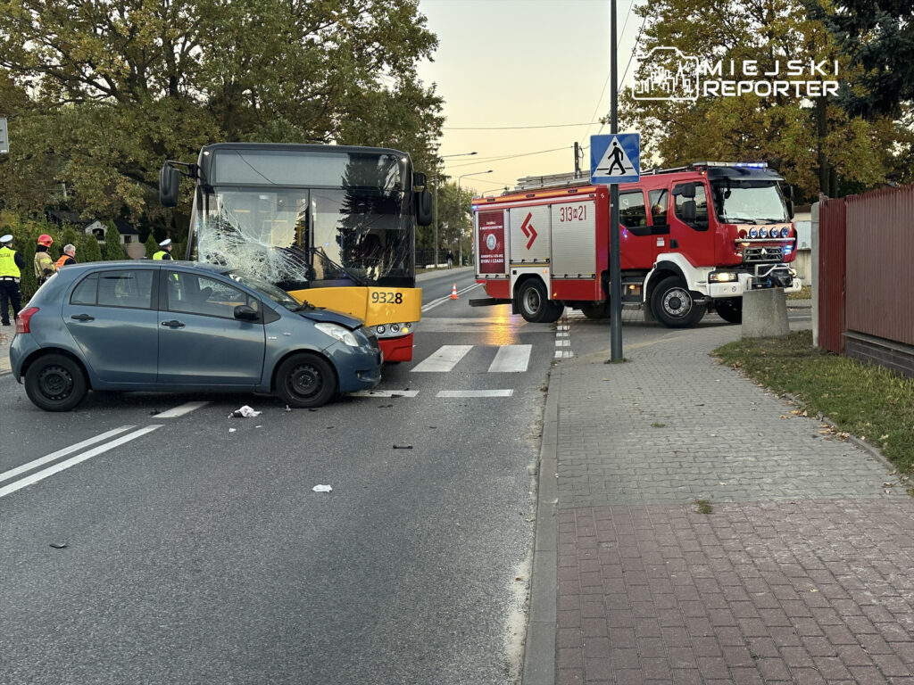 Zderzenie samochodu osobowego z autobusem miejskim na skrzyżowaniu, obok straż pożarna i ekipa ratunkowa.