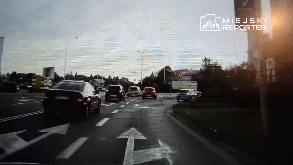 Ruch samochodowy na skrzyżowaniu, z pojazdami w różnych kierunkach, na drodze z wyznaczonymi pasami.