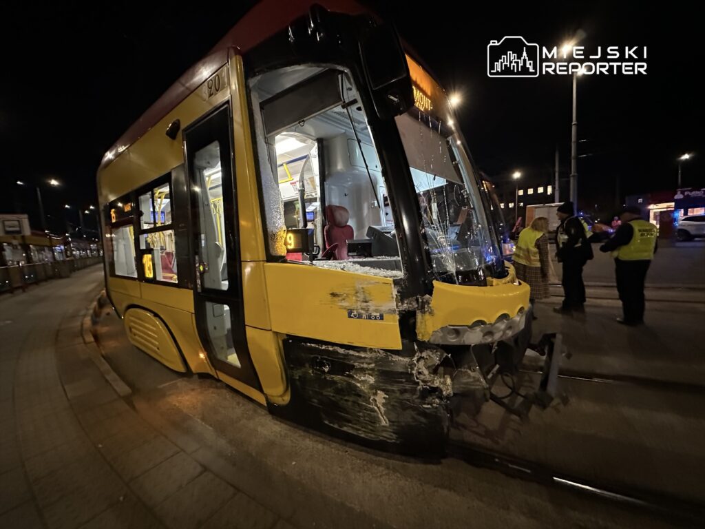 Zniszczony tramwaj z uszkodzoną przednią częścią stoi na przystanku, obok grupy policjantów i świadków zdarzenia.