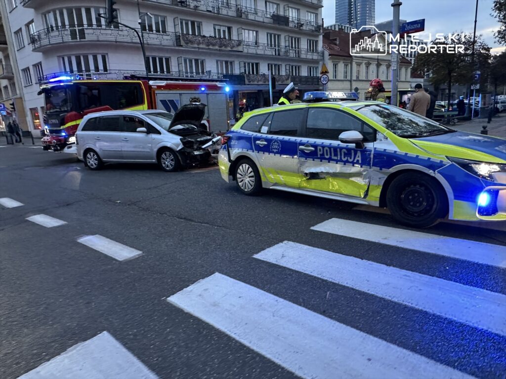 Wypadek drogowy z udziałem dwóch samochodów, w tym pojazdu policyjnego, na ulicy z przejściem dla pieszych.