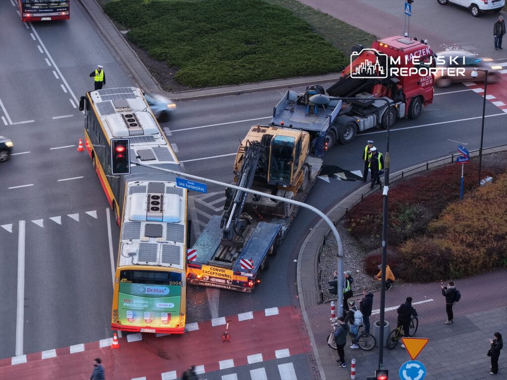 Kierowca autobusu stoi obok zatrzymanego pojazdu na skrzyżowaniu, podczas gdy policjanci kierują ruchem.