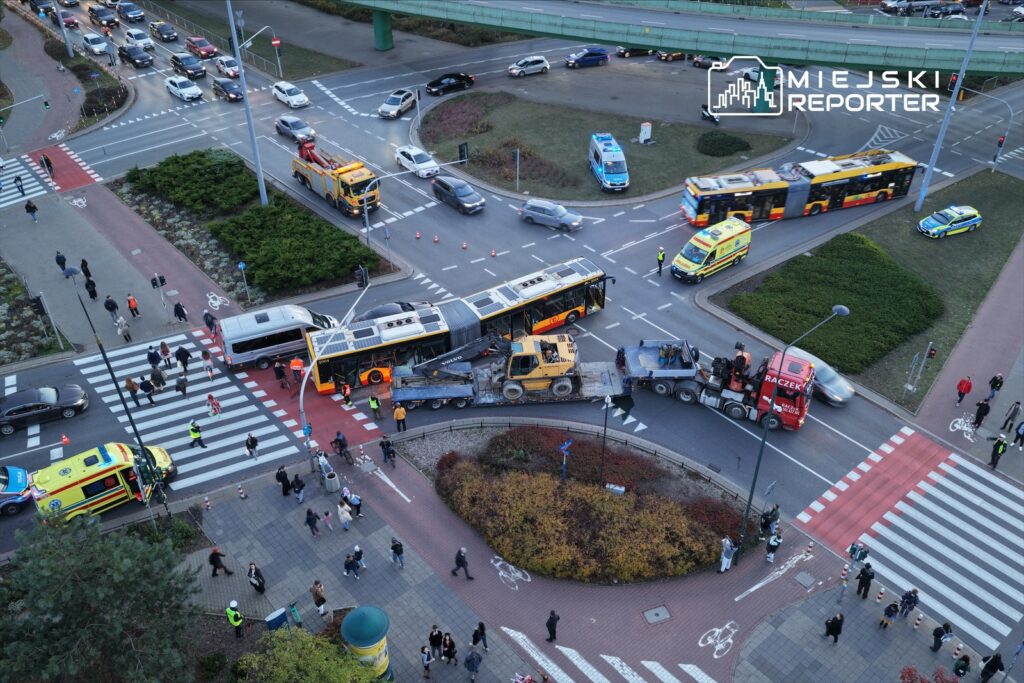 Wielki wypadek drogowy z udziałem autobusu i pojazdów ciężarowych na ruchliwym skrzyżowaniu. Policja i służby ratunkowe zabezpieczają miejsce zdarzenia.
