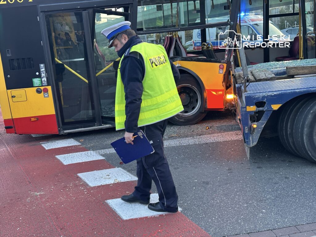 Policjant w kamizelce odblaskowej bada wypadek drogowy obok uszkodzonego autobusu na skrzyżowaniu.
