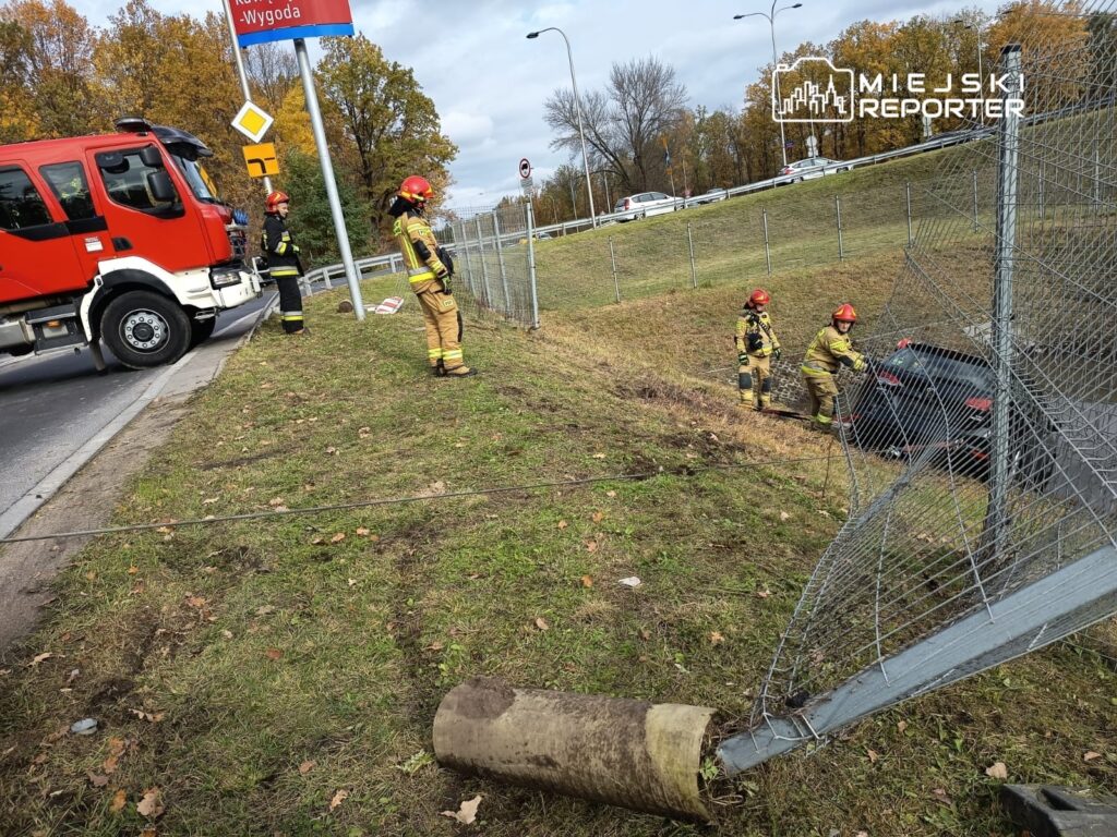 Czterech strażaków w mundurach pracuje przy wypadku drogowym, wyciągając samochód z rowu obok jezdni.