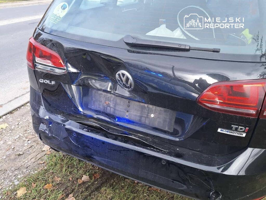 Uszkodzony czarny Volkswagen Golf z wgniecionym tyłem zaparkowany na poboczu drogi.