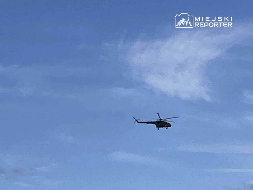 Helikopter przelatujący przez niebo z niewielkimi chmurami w tle.