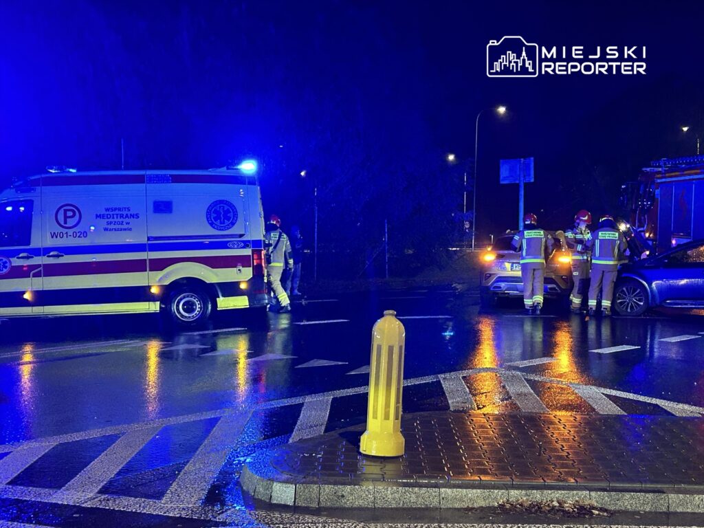 Zespół ratunkowy w mundurach omawia sytuację obok karetki na deszczowej ulicy nocą.