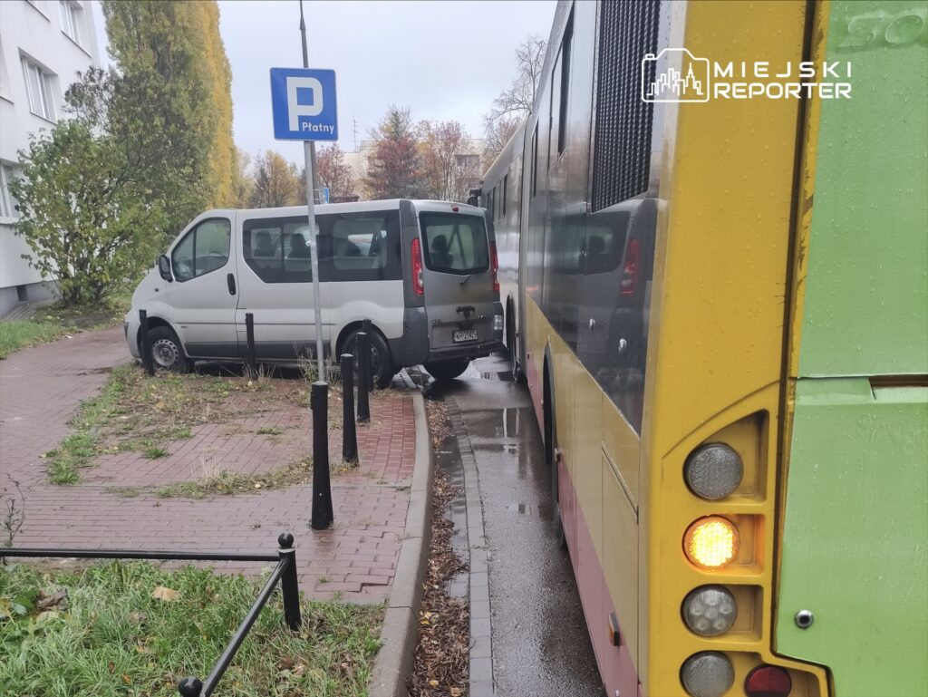 Zielony autobus stojący obok szarego vana na wąskiej ulicy, z widocznym znakiem parkingowym w tle.