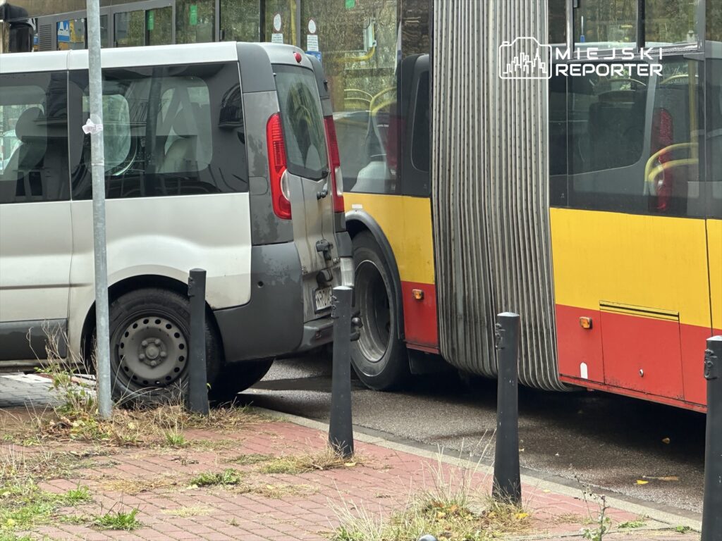 Biały samochód dostawczy stojący blisko przystanku, obok dużego autobusu komunikacji miejskiej.