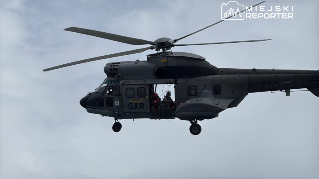 Śmigłowiec ratunkowy SAR przelatuje nad chmurami, z trzema członkami załogi siedzącymi na pokładzie.