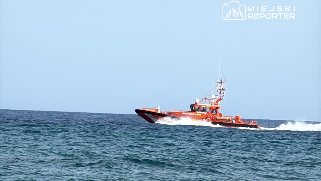 Czerwony kuter ratunkowy porusza się po falach morza, zostawiając za sobą białą pianę.