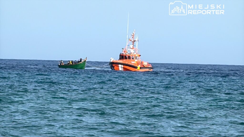 Czerwony kuter rybacki holuje zieloną łódź z grupą ludzi na morzu przy spokojnej wodzie.