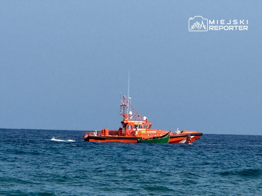 Łódź ratunkowa w pomarańczowym kolorze przemieszcza się po spokojnym morzu, w tle błękitne niebo.