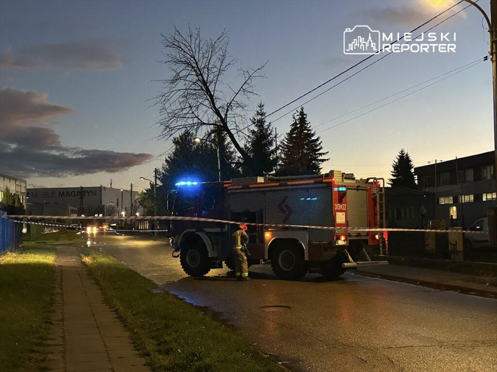 W nocy straż pożarna z niebieskimi światłami stoi na ulicy, zabezpieczając teren przy magazynie meblowym.