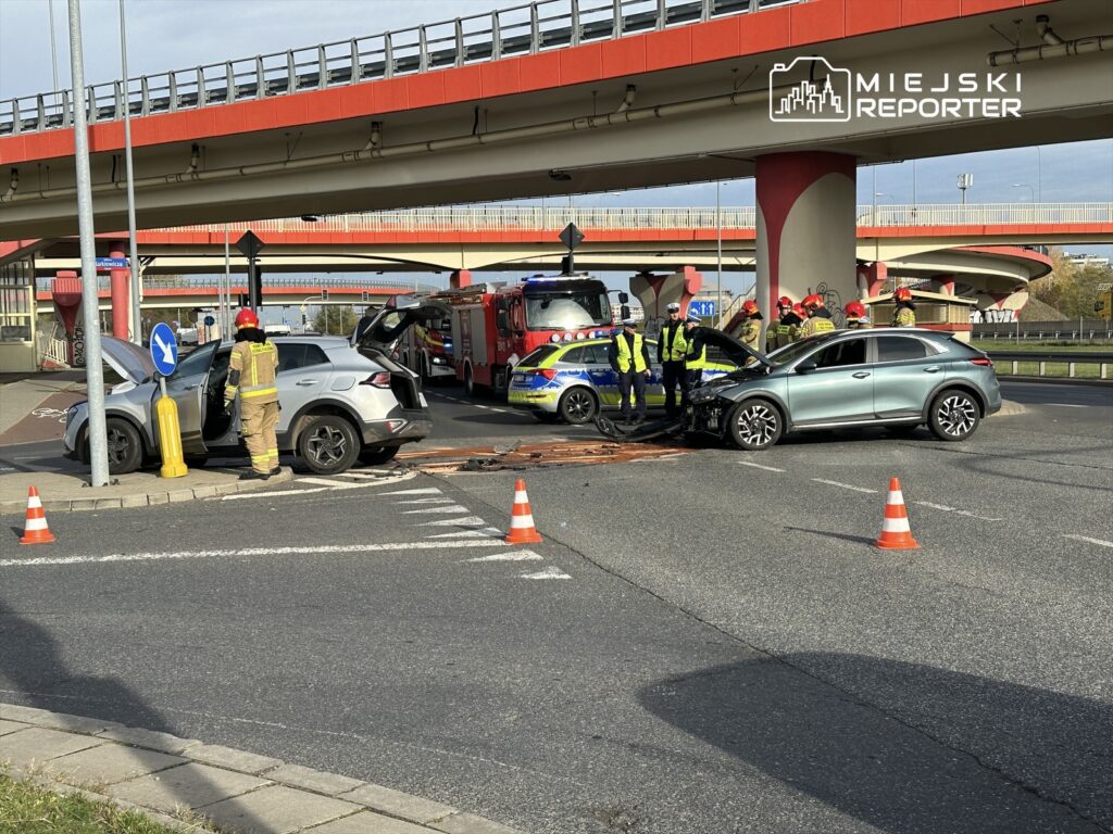 W miejscu wypadku drogowego strażacy i policjanci pracują nad zabezpieczeniem pojazdów oraz udzielaniem pomocy poszkodowanym.