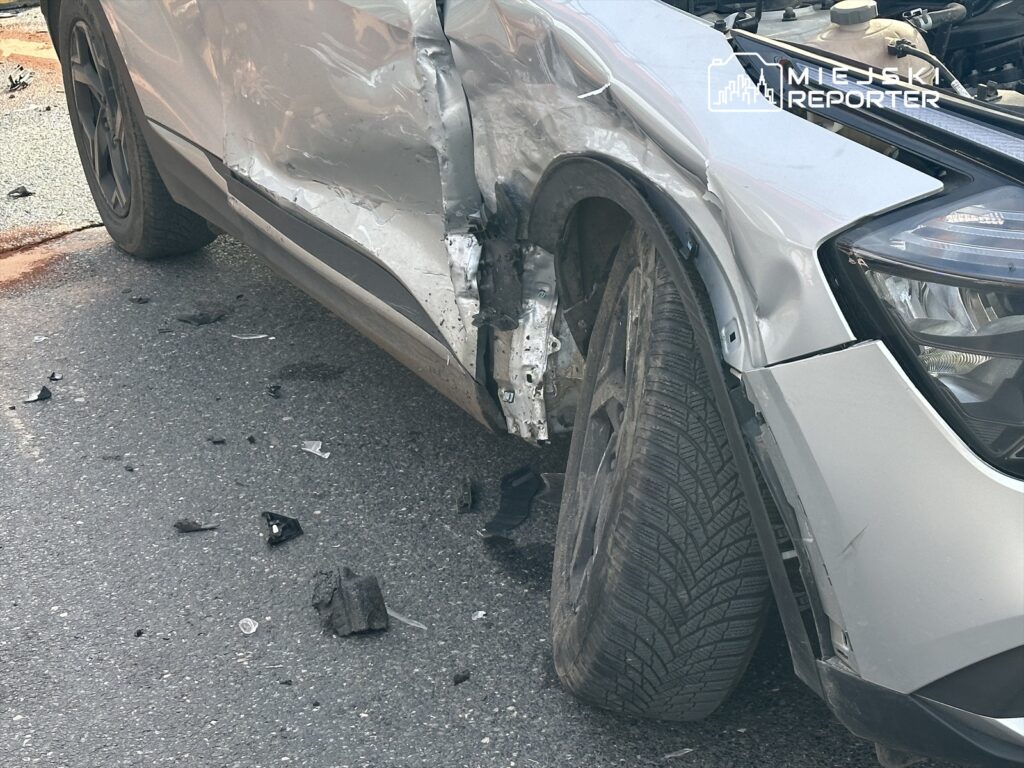 Uszkodzony samochód osobowy z wgniecioną przednią częścią stoi na drodze, obok leżą fragmenty plastików.