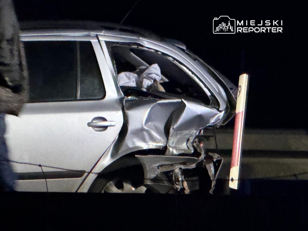 Uszkodzony samochód osobowy z wgniecioną tylną częścią, zaparkowany w ciemnej okolicy.