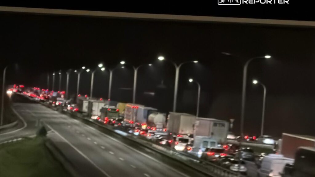 Długi korek samochodowy na drodze, z widocznymi światłami pojazdów w nocy.