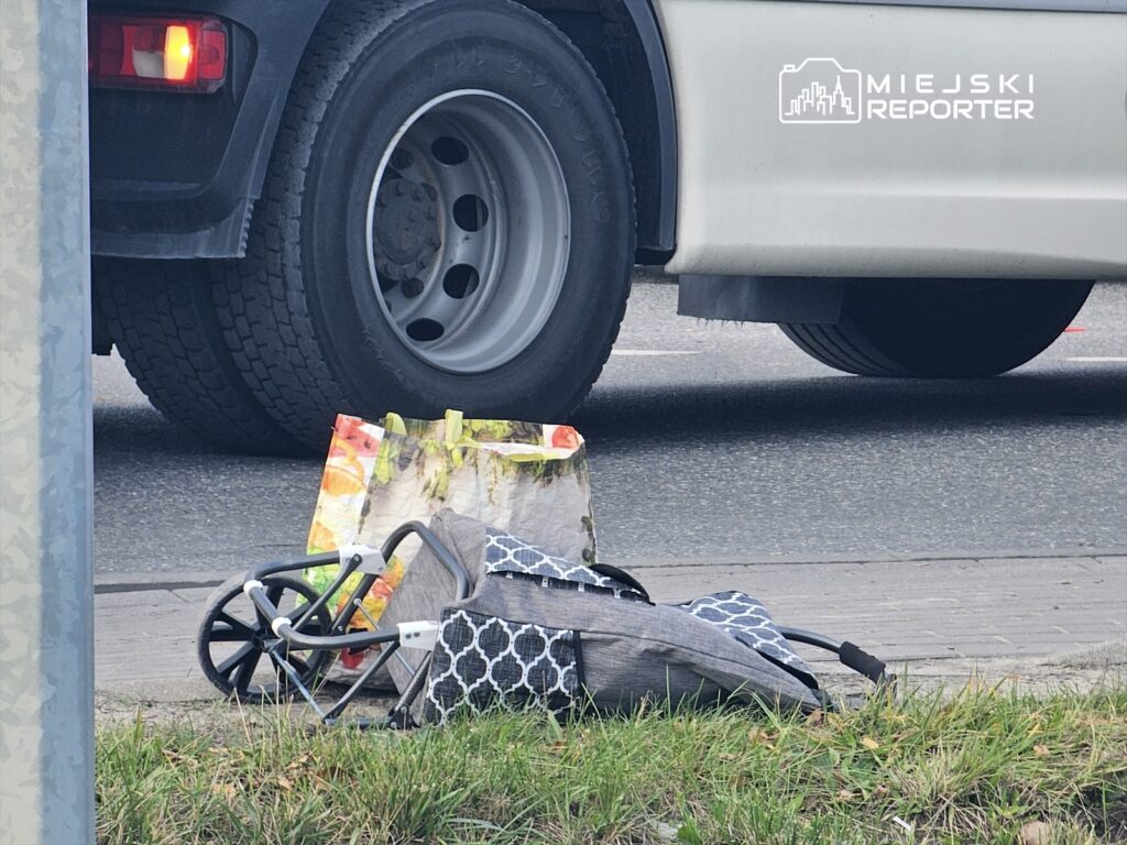 Wózek dziecięcy i torba leżą na chodniku obok dużego pojazdu ciężarowego.