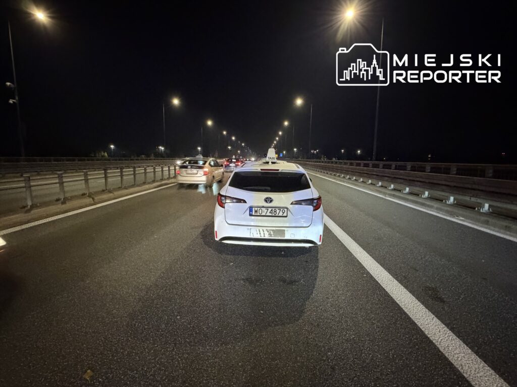 Ruch samochodów na oświetlonej autostradzie w nocy, widok z tylnej perspektywy białego pojazdu.