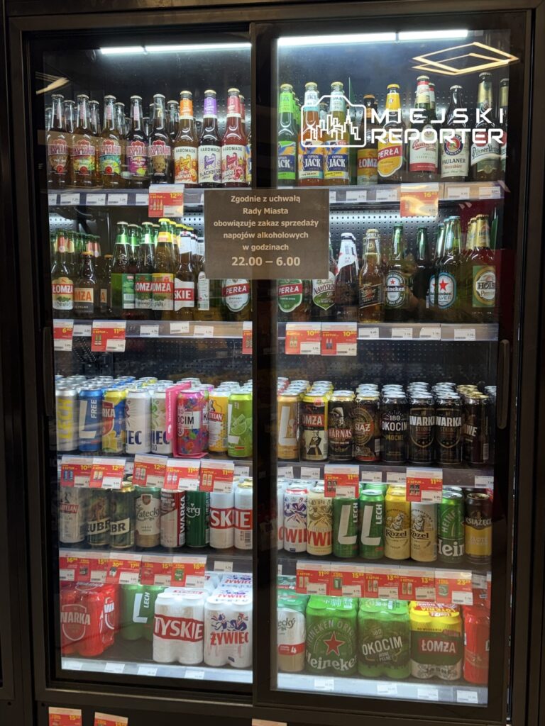 Półka z różnymi rodzajami napojów alkoholowych w sklepie, z widocznymi cenami i informacją o zakazie sprzedaży w godzinach nocnych.
