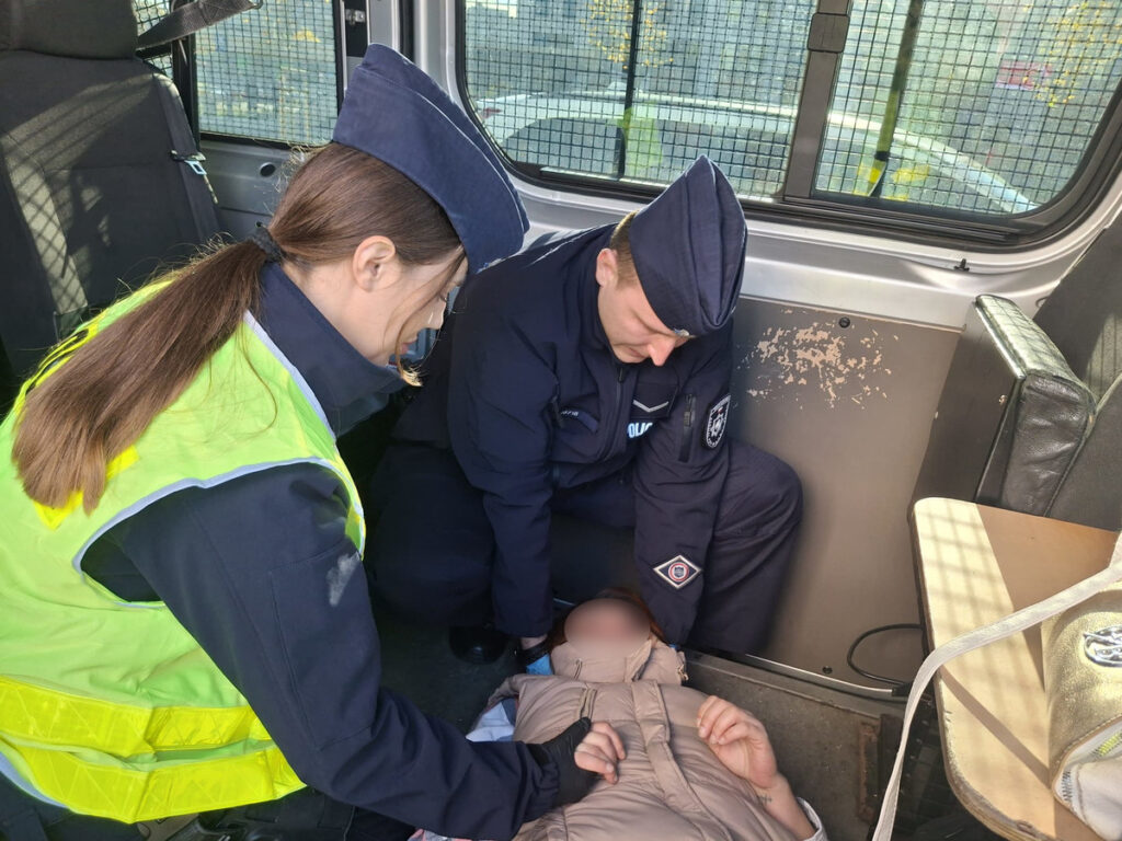 Dwóch funkcjonariuszy policji udziela pomocy osobie leżącej na podłodze w radiowozie.