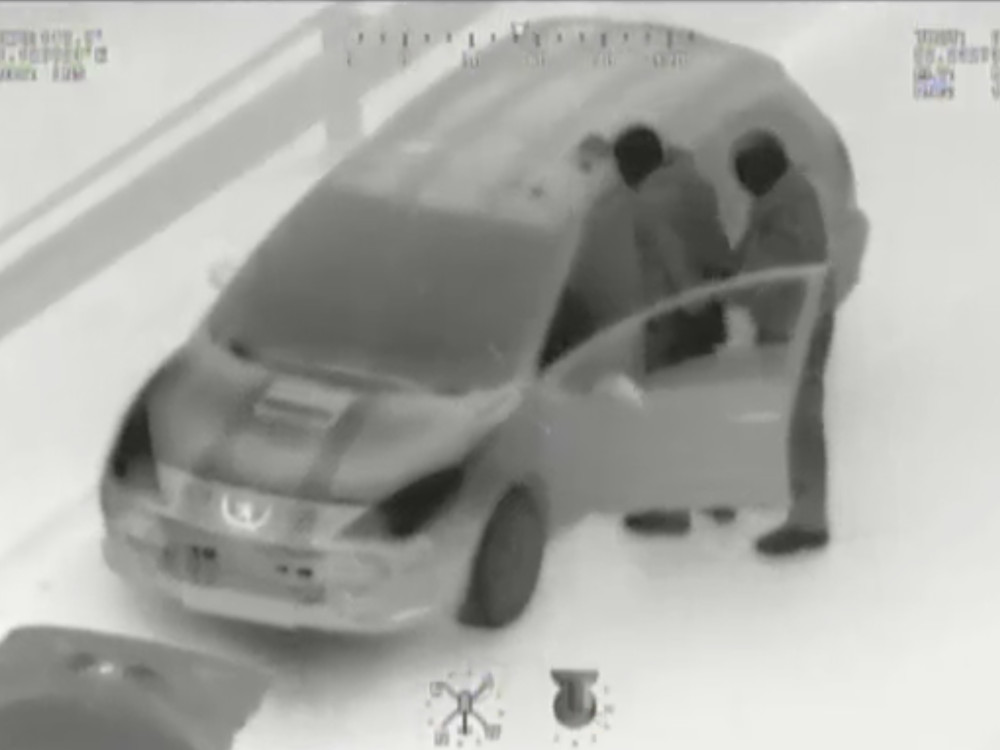 Dwóch mężczyzn przy otwartych drzwiach samochodu osobowego na ośnieżonej drodze.