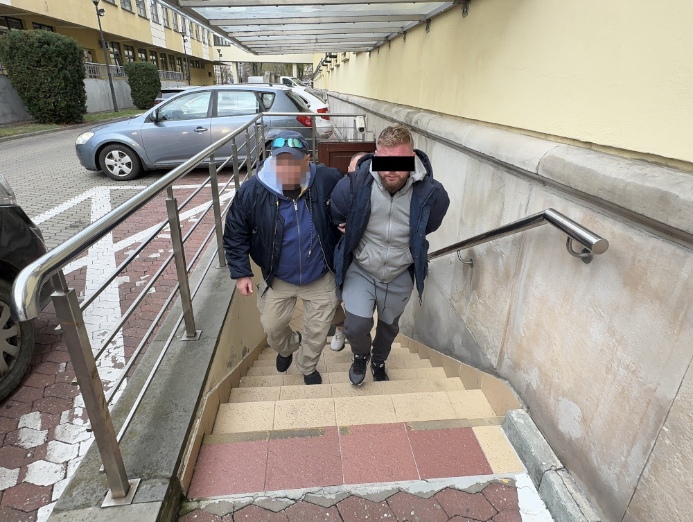 Dwóch mężczyzn schodzi po schodach wzdłuż poręczy, w tle zaparkowane samochody.