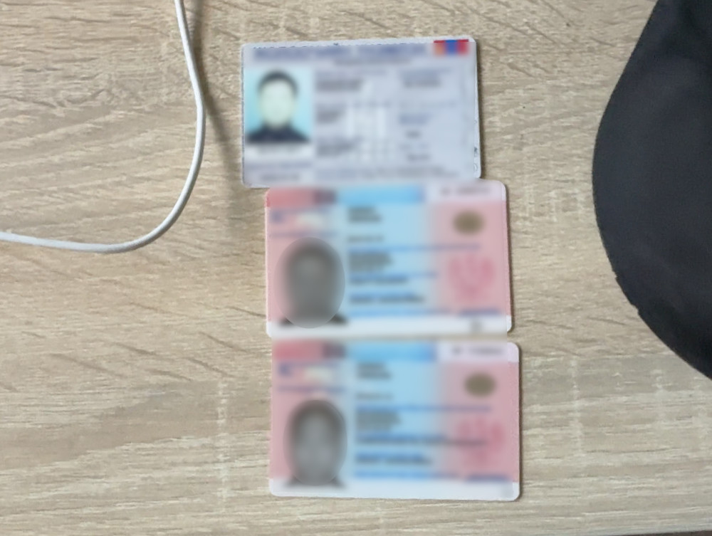 Trzy dowody osobiste leżące na drewnianym stole, z kablem widocznym obok.