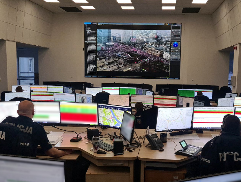 Funkcjonariusze policji pracują w centrum operacyjnym, monitorując wydarzenia na dużych ekranach.