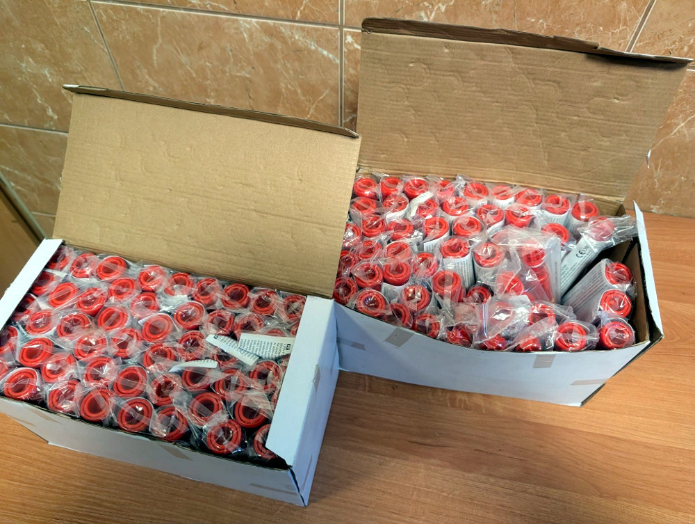 Dwie otwarte kartony wypełnione czerwonymi fiolkami, umieszczonymi w przezroczystych opakowaniach.