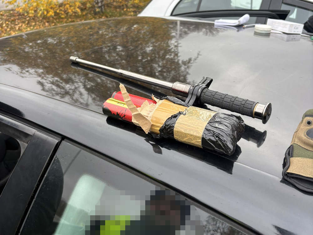 Na masce samochodu leży pałka i pakunek owinięty w czarny materiał, obok rękawica taktyczna.