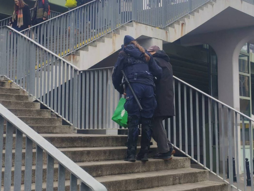 Funkcjonariusz policji pomaga osobie w pokonywaniu schodów w miejskim otoczeniu.