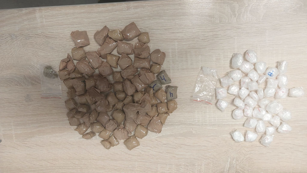 Na blacie leżą pakunki z substancjami, w tym brązowe i białe woreczki. W centrum widoczne są numery i litery na brązowych pakunkach.