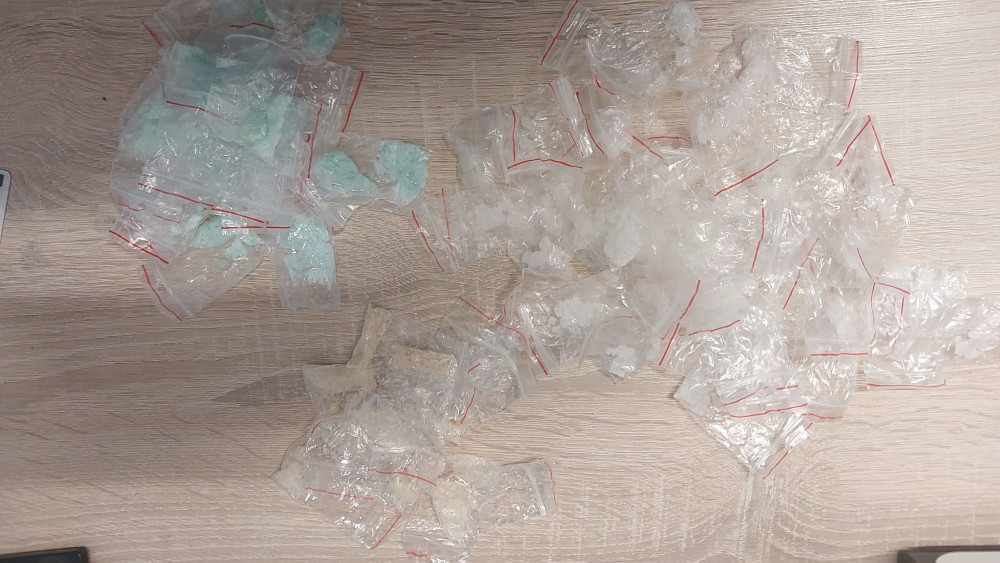 Pakiety z substancjami w różnych kolorach leżą na drewnianym stole, niektóre są przezroczyste, inne zielone.