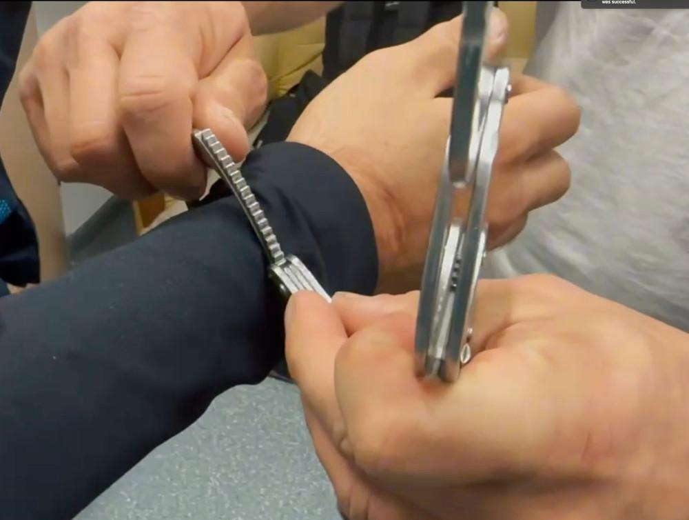 Mężczyzna w niebieskiej koszuli trzyma rękę innego mężczyzny, podczas gdy ten zakłada mu kajdanki.