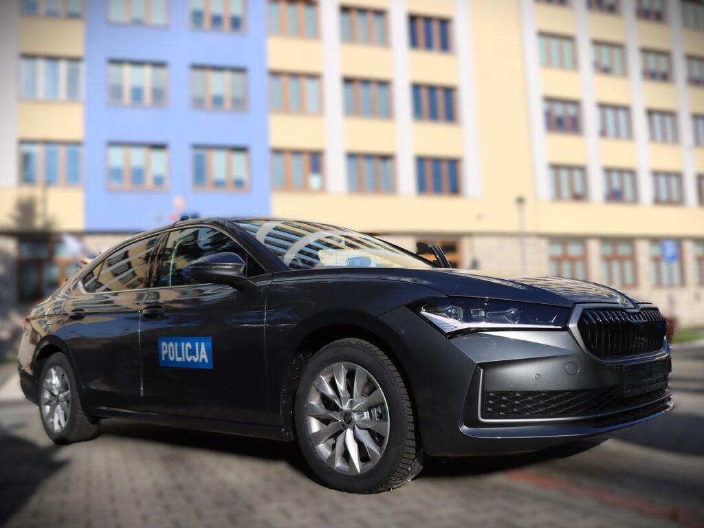 Czarny radiowóz z napisem "POLICJA" zaparkowany przed budynkiem z kolorową elewacją.