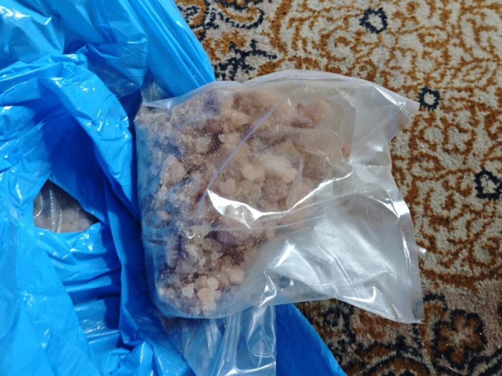 Pakiet z substancją sypką leży na wzorzystym dywanie obok niebieskiej torby.