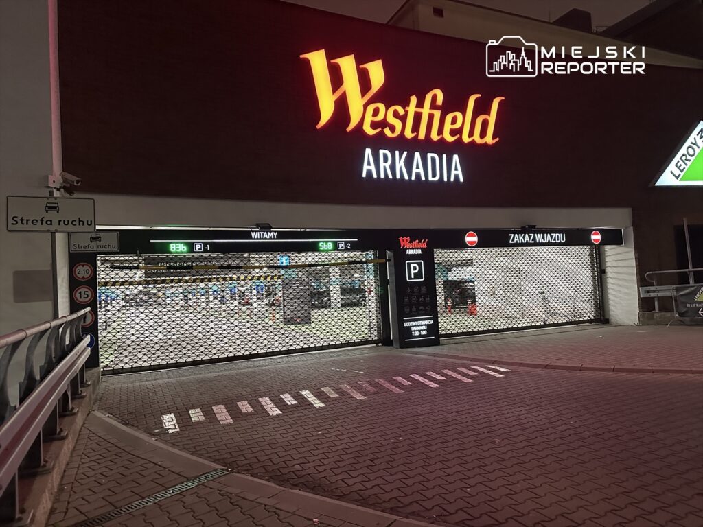 Zamknięty wjazd do parkingu w centrum handlowym Westfield Arkadia, z widocznymi znakami drogowymi i siatką.